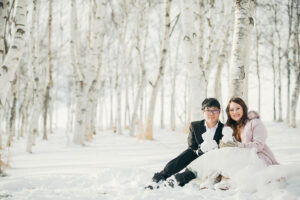 雪の積もる白樺並木の前に座って正面を向いている新郎新婦