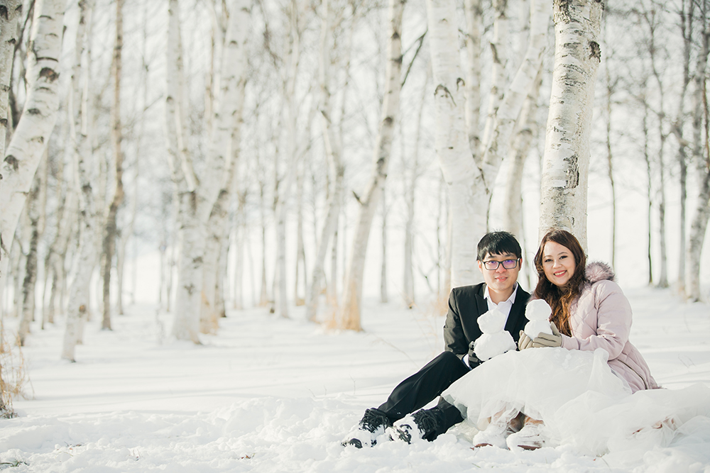 雪の積もる白樺並木の前に座って正面を向いている新郎新婦