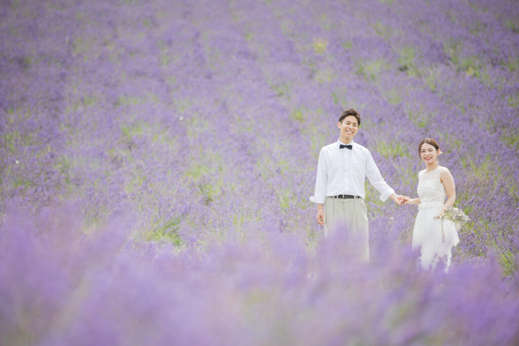ラベンダー畑で手を繋いで正面を向いている新郎新婦
