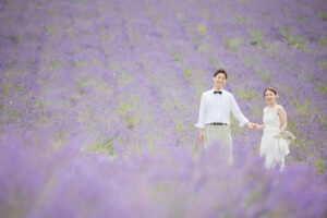 ラベンダー畑で手を繋いで正面を向いている新郎新婦