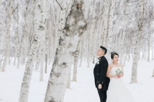 冬の白樺並木の前に立つ新郎新婦